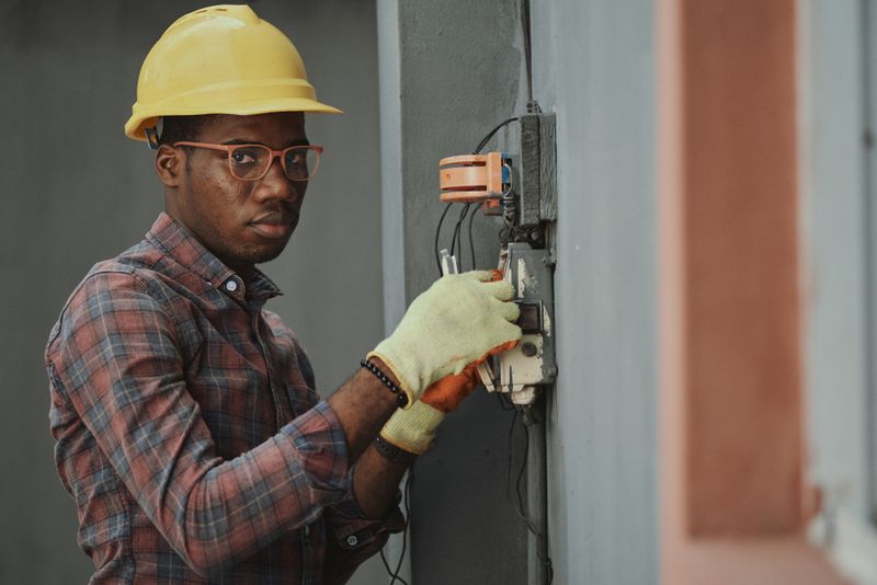 Electrician in a yellow hard hat wiring a control box on a job site