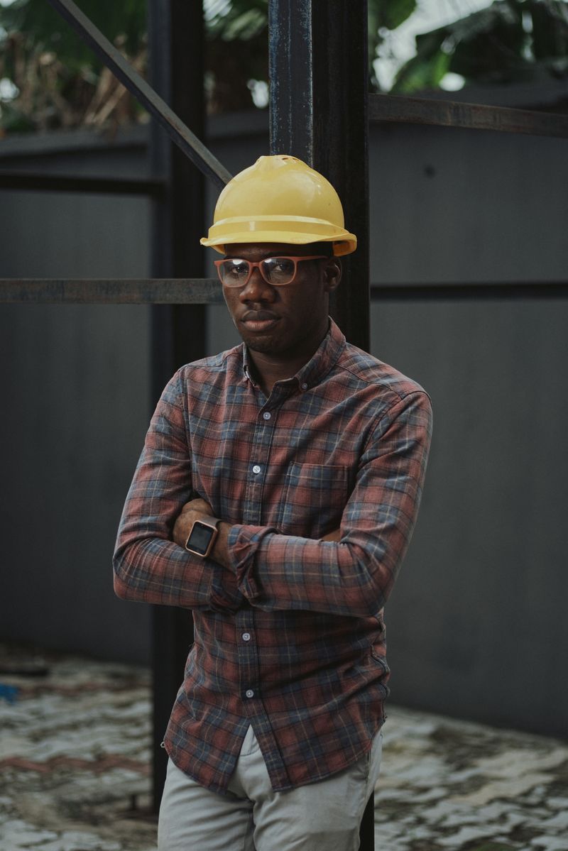 Electrician in a yellow hard hat and plaid shirt standing at a job site, arms crossed
