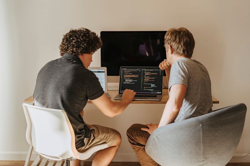 Two developers pair-programming at a desk with code on the screens